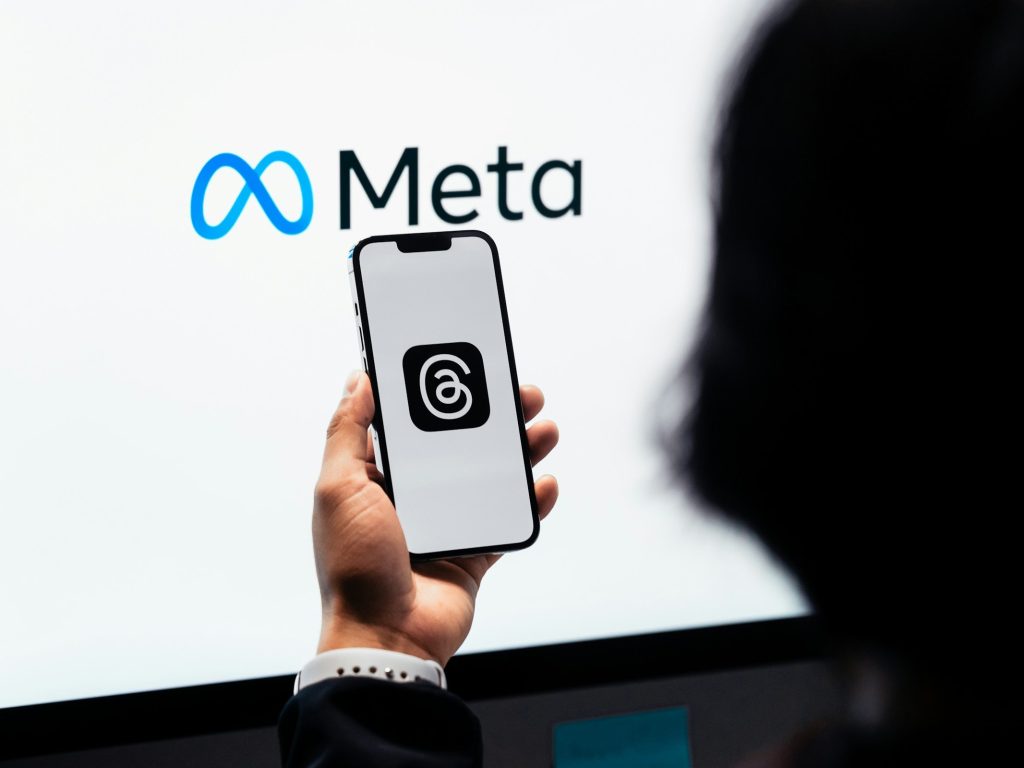 Person holding a phone displaying the Threads social media platform in front of the Meta logo as the company confirms plans to utilise content shared by its adult users in the EU (European Union) on platforms like Instagram and Facebook to train its AI models.