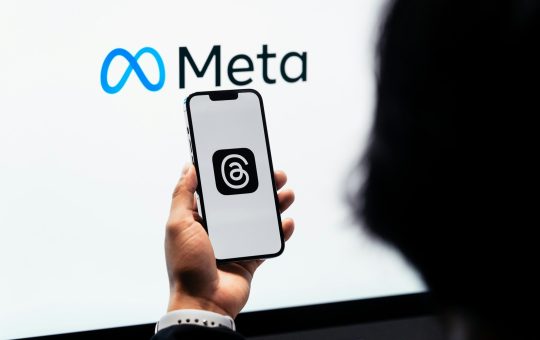 Person holding a phone displaying the Threads social media platform in front of the Meta logo as the company confirms plans to utilise content shared by its adult users in the EU (European Union) on platforms like Instagram and Facebook to train its AI models.